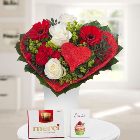 Blumenstrauß als Herz mit weißen Rosen und roten Germini dazu ein roter HErzstecker eine Grußkarte und eine Merci Schokolade
